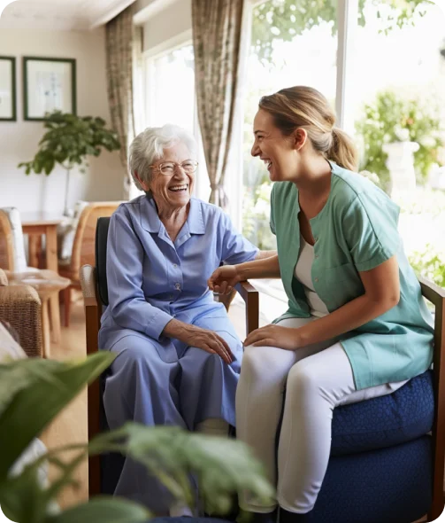 Lächelnde Pflegerin im Gespräch mit einer älteren Patientin in einem Wohnzimmer in Iserlohn